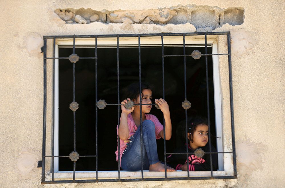 طفلتان خلف نافذة منزل بجنوب قطاع غزة يتابعن جنازة الفلسطيني عبد الله عبد العال