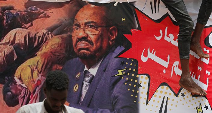 متظاهر يقف أمام لافتة تصور الرئيس السوداني السابق عمر البشير أمام وزارة الدفاع في الخرطوم