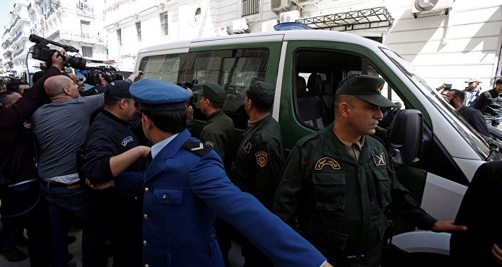 وسائل الإعلام والشرطة تحيط بقافلة من مركبات الشرطة بينما يتم نقل رجل أعمال مشتبه به إلى المحكمة في الجزائر